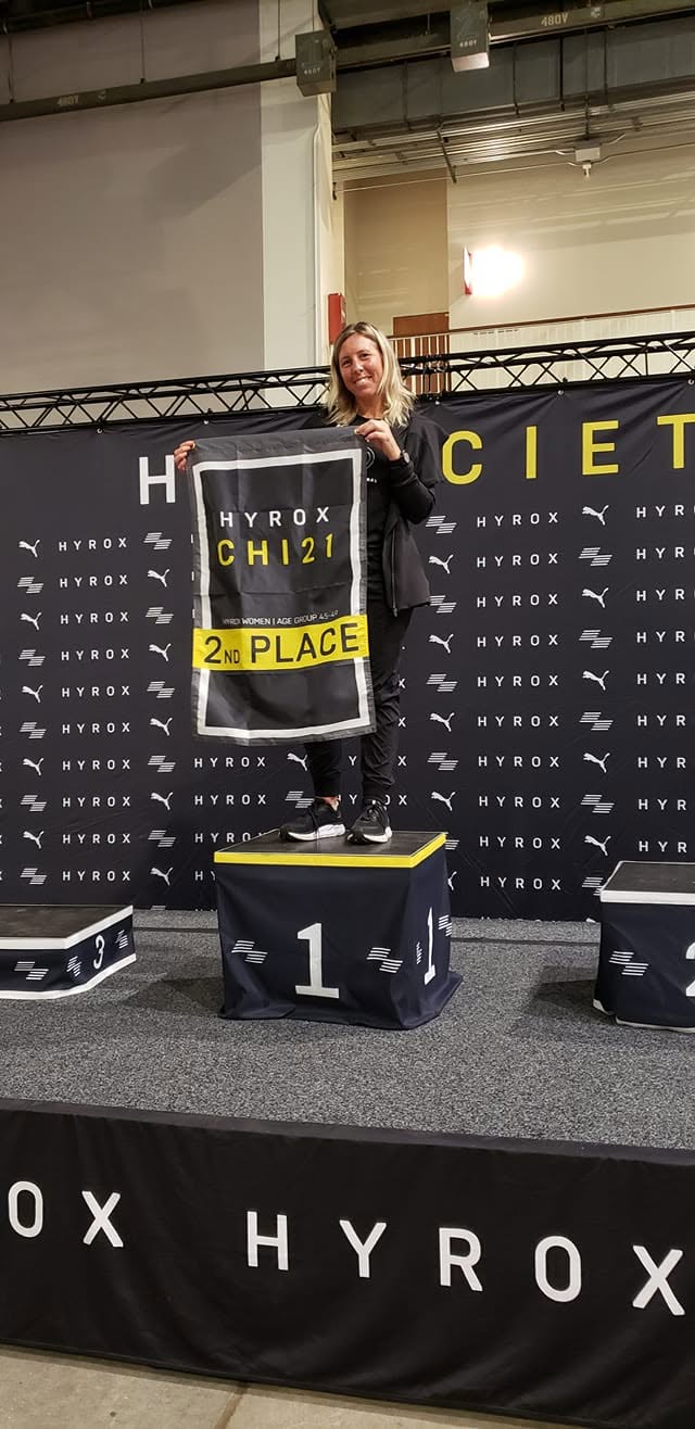 A Ruckhouse Athletics member holding her 2nd place age group banner on the podium at HYROX Chicago